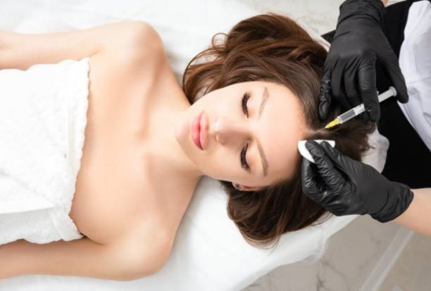 Mesotherapy,  vitamin injections in head skin of hair area. Professional hair loss treatment. Close up view of woman head and doctor's hands with syringe. View above.